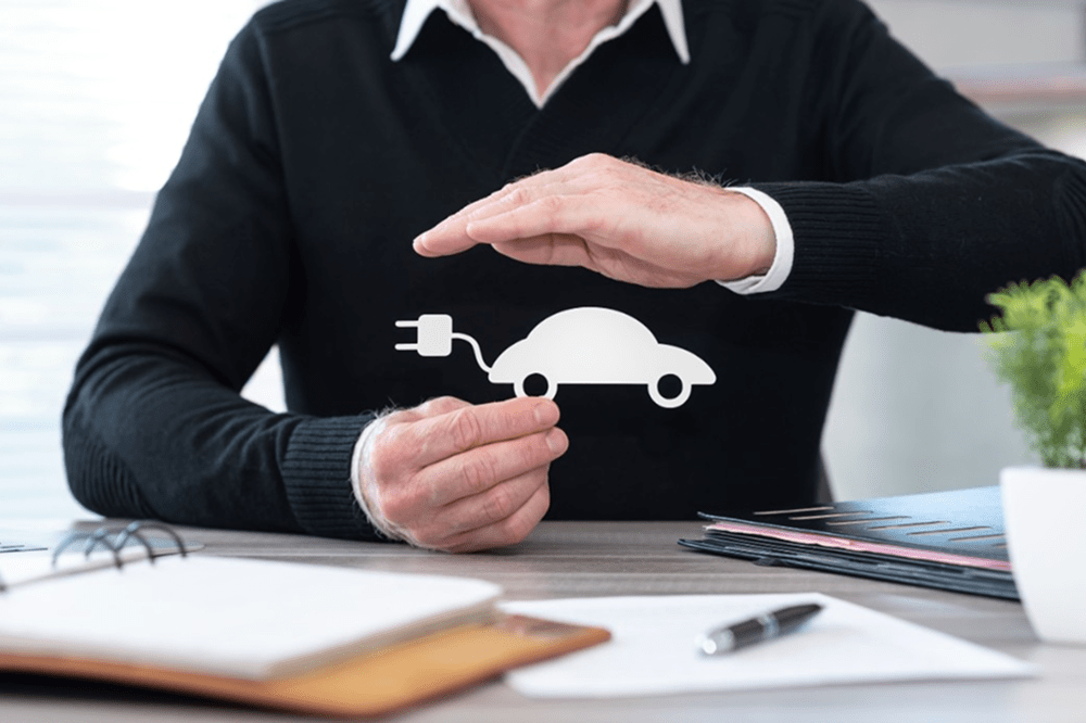 Pessoa simbolizando proteção com as mãos sobre um ícone de carro elétrico