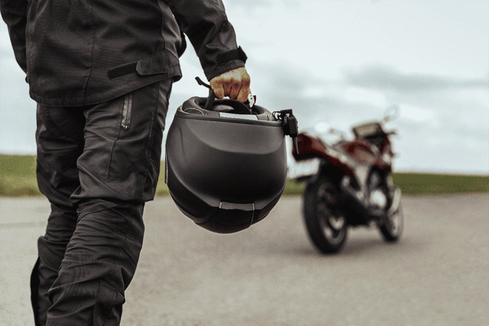Motociclista segurando capacete com moto estacionada ao fundo
