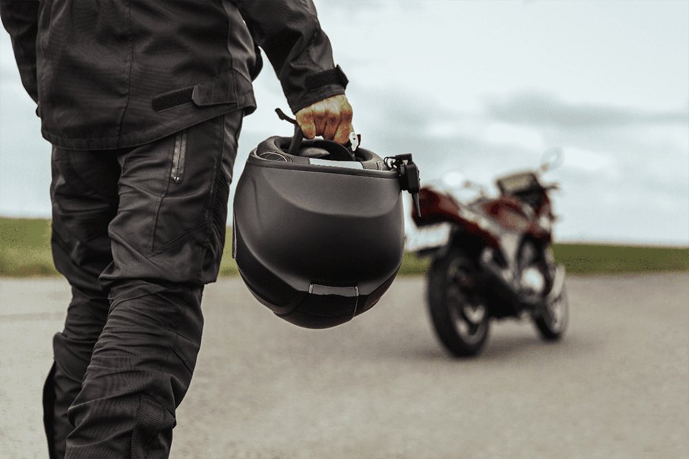 Motociclista segurando capacete com moto estacionada ao fundo