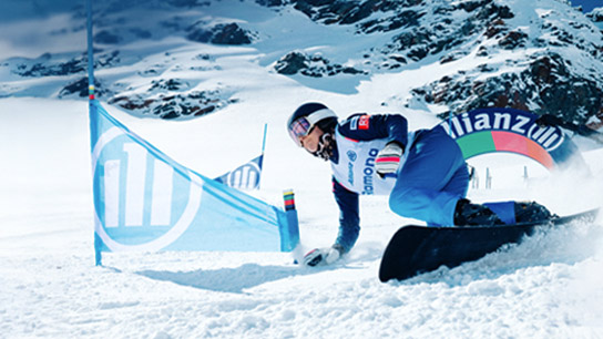 Atleta olímpico esquiando em montanha de neve com bandeiras e totem com logo da Allianz ao fundo