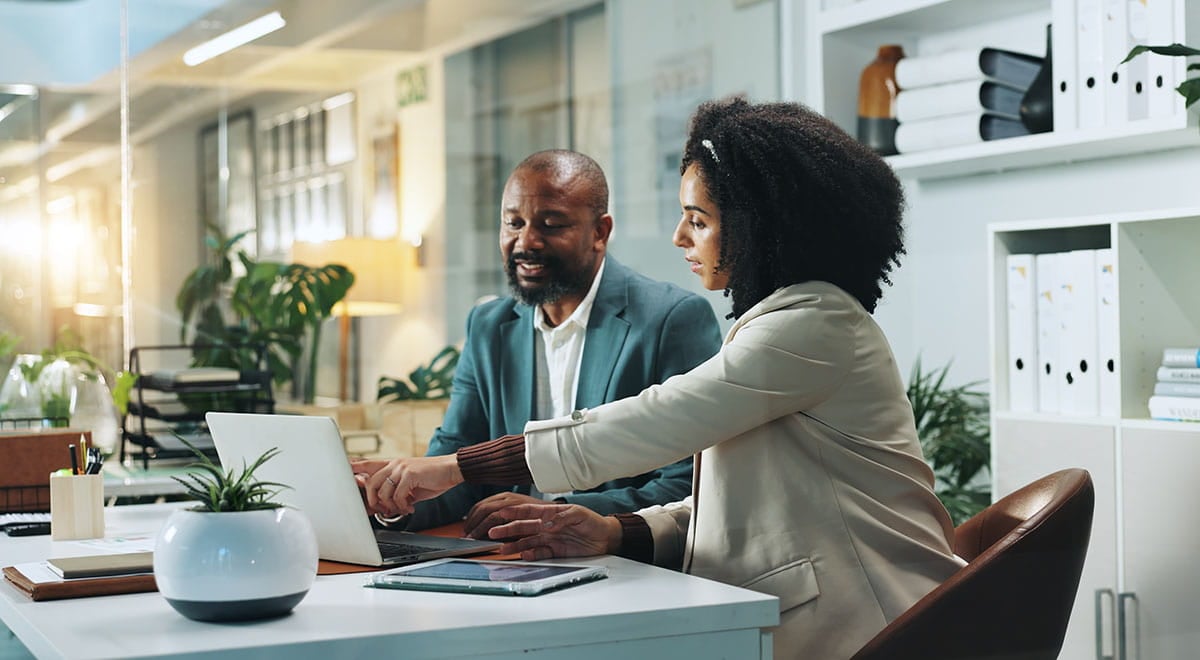 Homem e mulher sentados e conversando em mesa de escritório