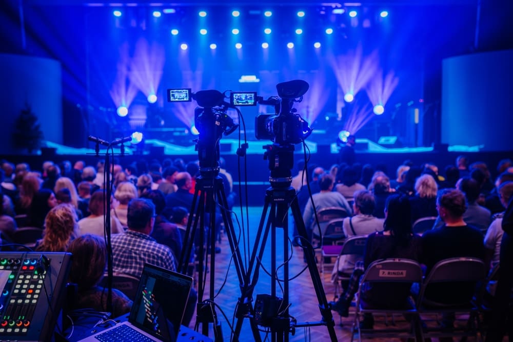 Plateia assistindo uma apresentação em um teatro com câmeras de filmagem