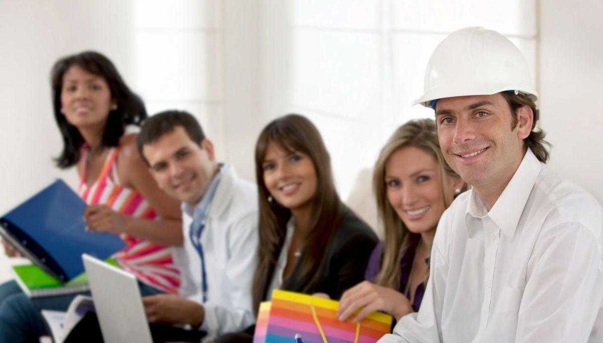 Um grupo de 5 profissionais sentados em uma fileira. Um dos homens, à direita, veste um capacete branco de segurança, os demais parecem representar profissionais administrativos ou comerciais.