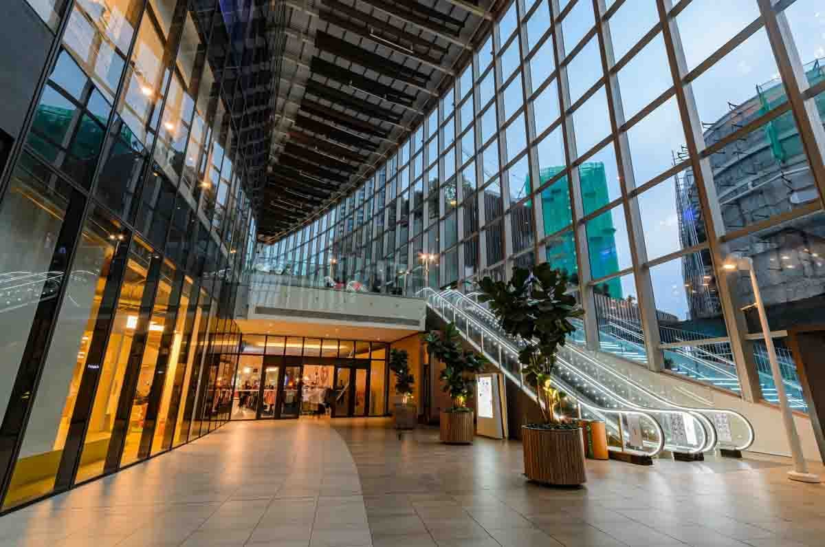 Interior de shopping contemporâneo com fachada envidraçada e escada rolante iluminada.