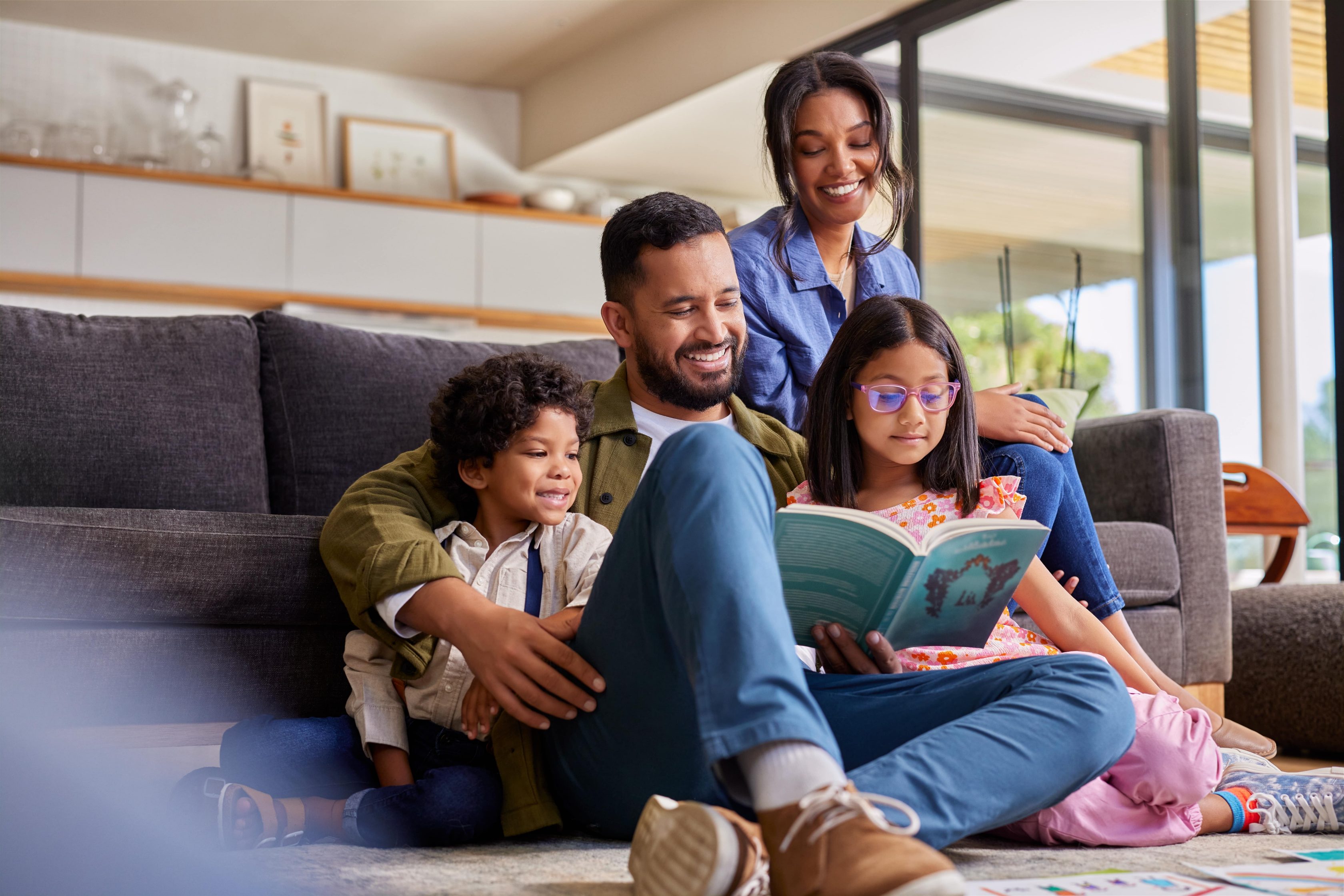 Família reunida no sofá lendo um livro, com atenção e carinho mútuo.