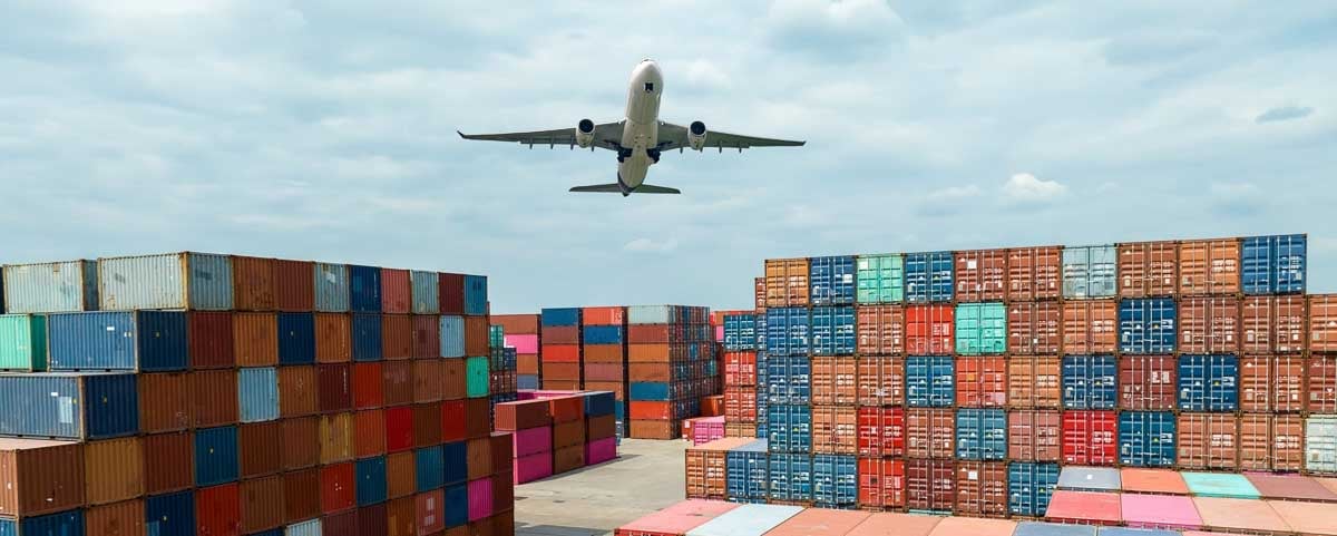 Avião sobrevoa terminal de contêineres, representando conexão entre modais logísticos.