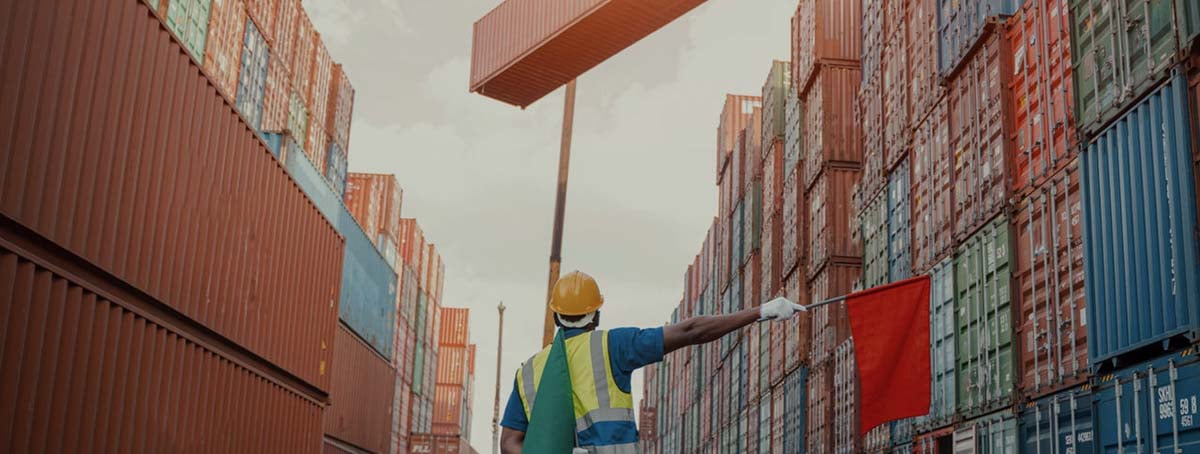 Imagem de um funcionário do porto auxiliando a grua a posicionar o contâiner