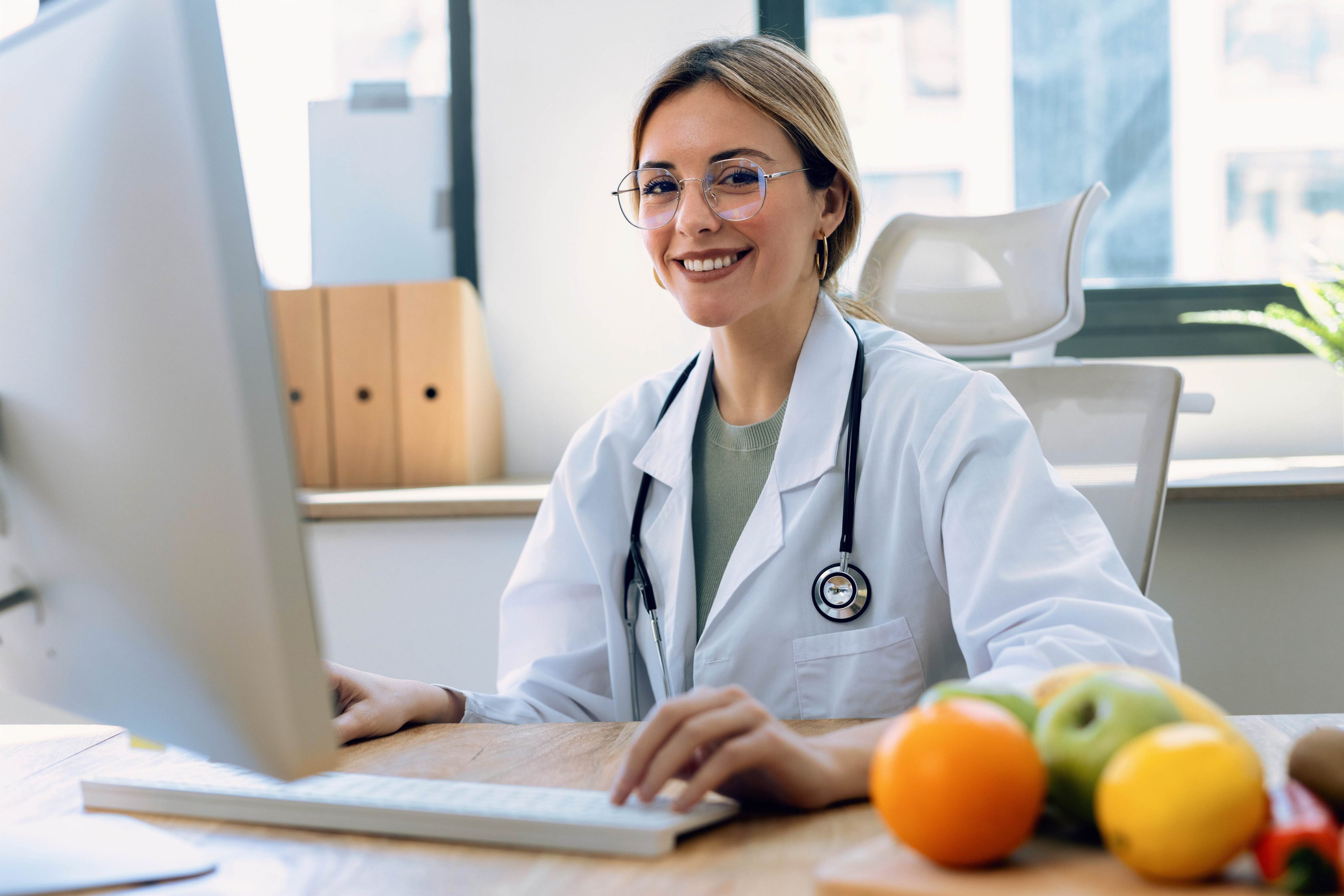 Nutricionista sentada e sorrindo em frente ao computador