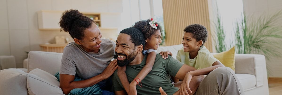 Família sentado no sofá e sorrindo, representando a proteção do seguro de vida Allianz