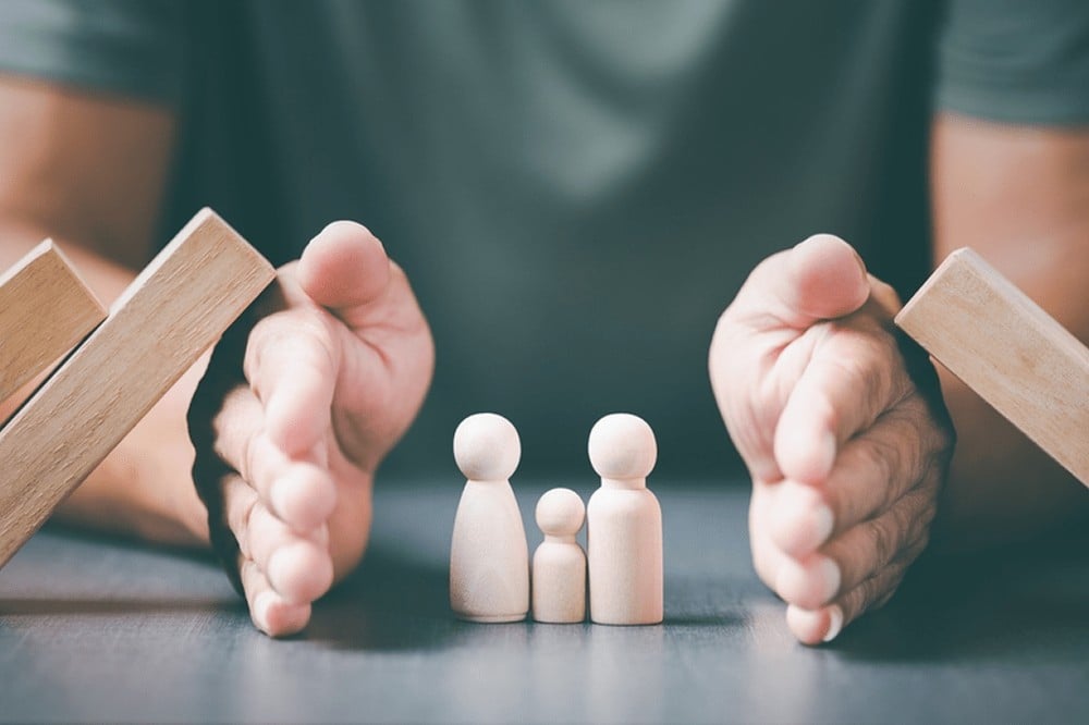 Mãos de um homem protegendo bonecos de madeira representando uma família de 3 pessoas