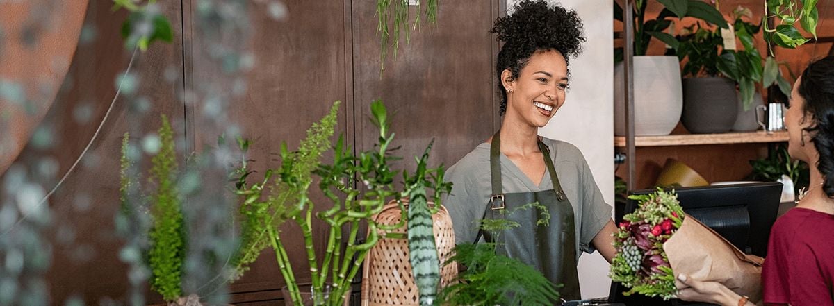 Atendente de uma floricultura entregando flores para uma cliente no balcão
