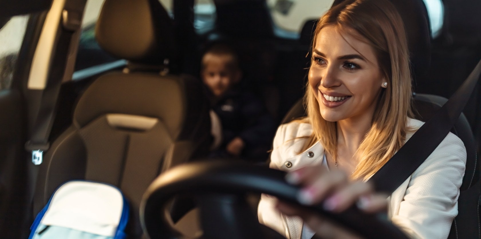 mulher dirigindo carro sorrindo com ouma criança no banco de trás