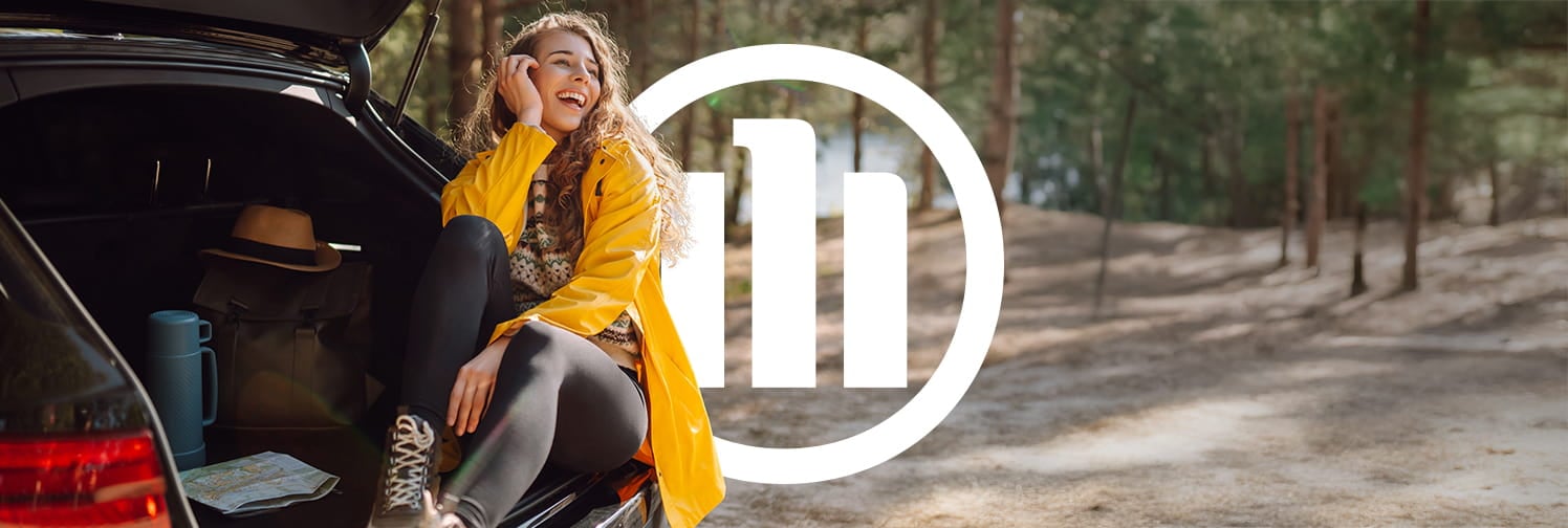 Mulher feliz em seu carro durante uma viagem, representando a cobertura do seguro Auto Allianz