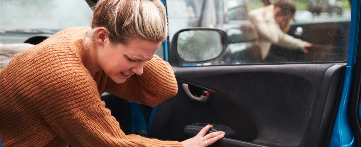 Imagem de uma mulher saindo do carro com a mão na nuca, logo após um sinistro. A imagem é ilustrada na parte que abordao conceito de dano corporal.