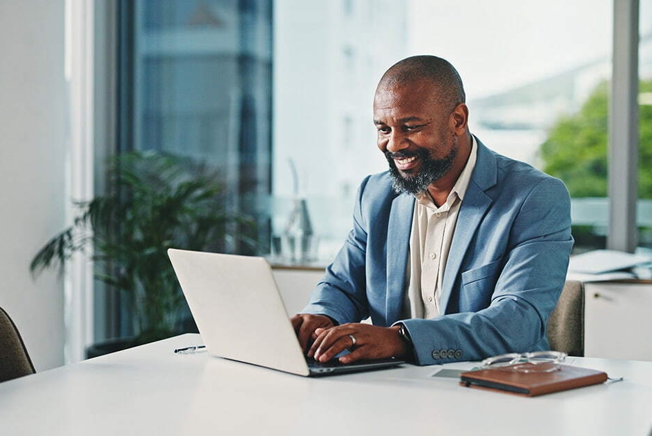 Homem trabalhando no escritório, usando notebook e sorrindo