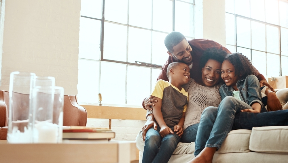 Família com pai, mãe e dois filhos sentados no chão da sala e sorrindo