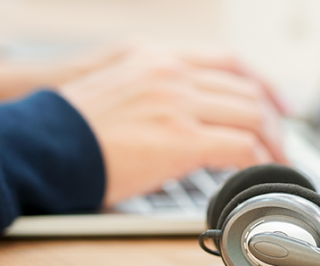 Imagem de uma pessoa utilizando o notebook ao lado de um fone de ouvido