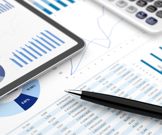 Imagem de uma mesa de escritório com uma caneta e ao fundo gráficos 