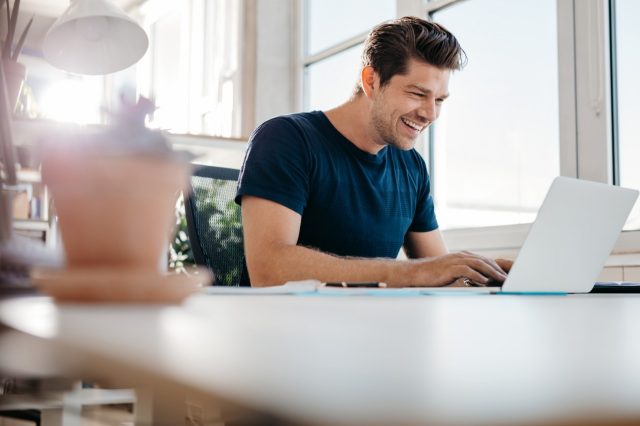 Homem utilizando o notebook e sorrindo