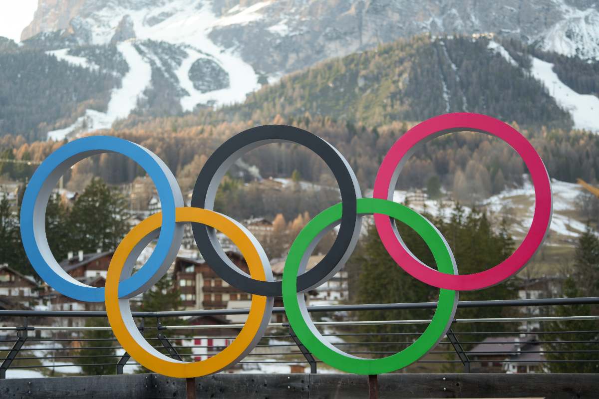 Anéis olímpicos instalados ao ar livre com montanhas nevadas ao fundo, simbolizando os Jogos Olímpicos de Inverno Milão‑Cortina 2026.