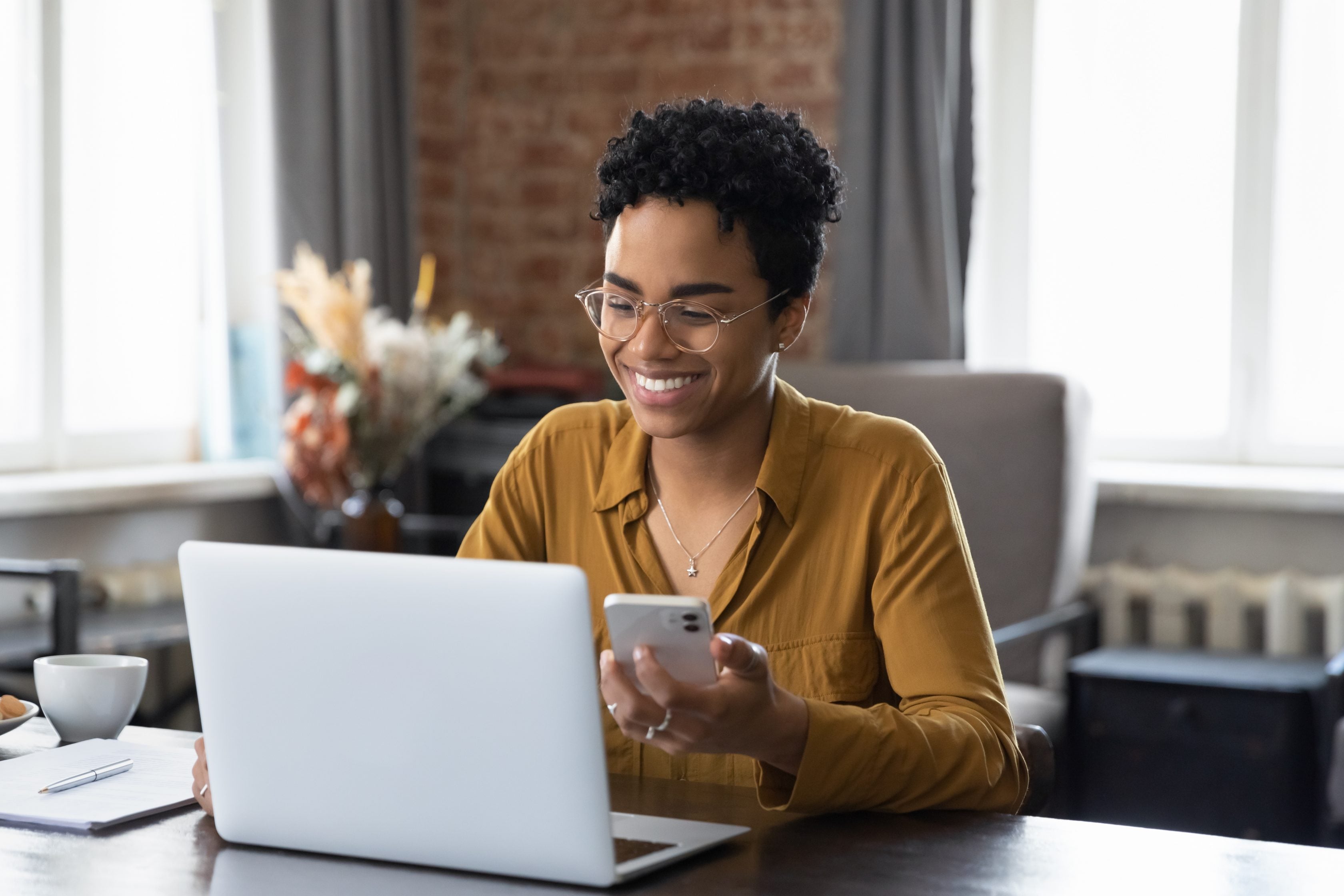 Corretora da Allianz sorrindo com o celular na mão utilizando o notebook