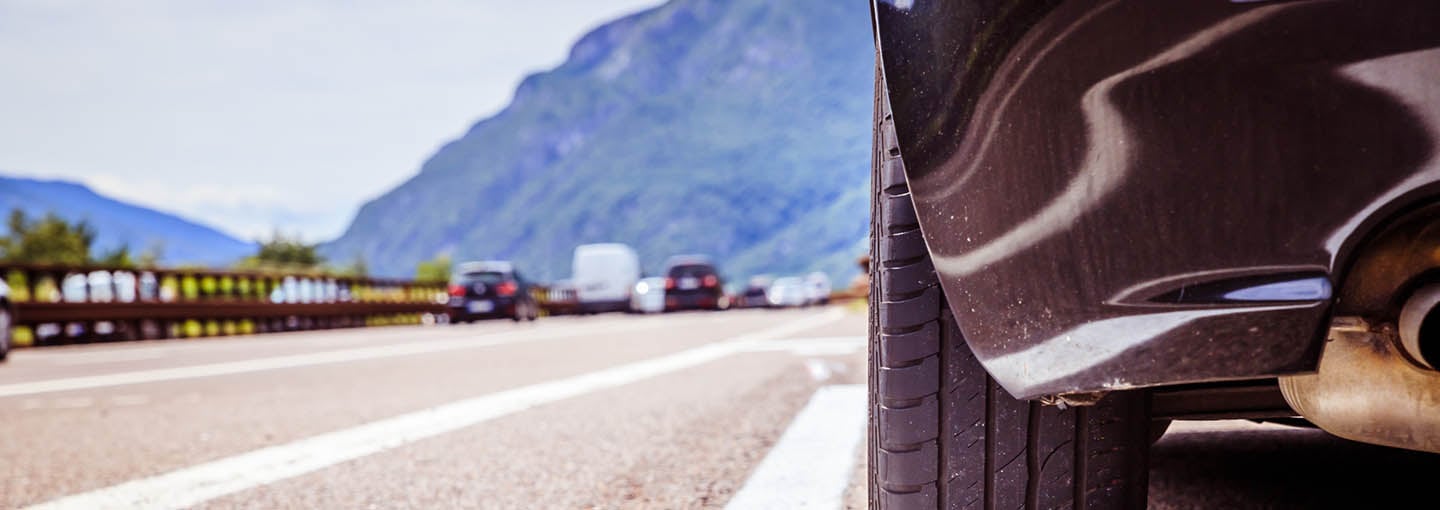 Imagem do pneu de um carro parado na estrada com montanhas ao fundo