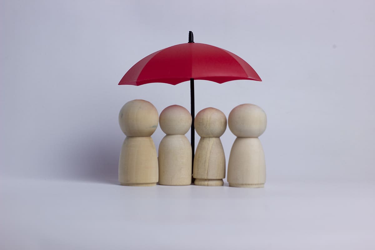Quatro figuras de madeira sob guarda-chuva vermelho simbolizando proteção