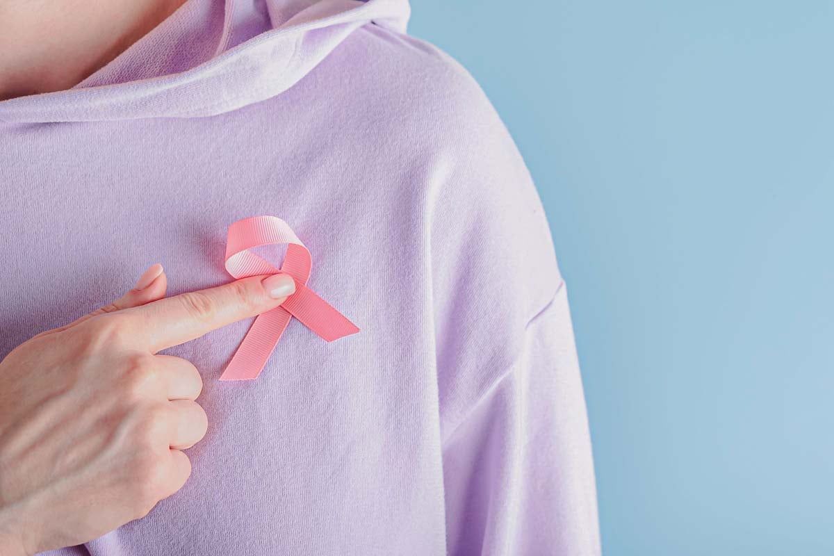 Imagem de uma mulher segurando uma fita cor de rosa na altura do peito