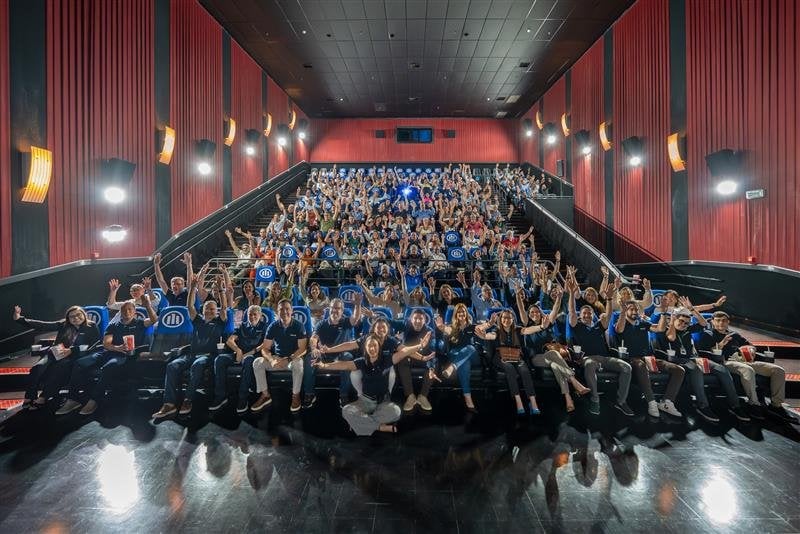 Grupo de profissionais reunidos em sala de treinamento, com participantes sentados e braços levantados durante capacitação promovida pela Allianz.