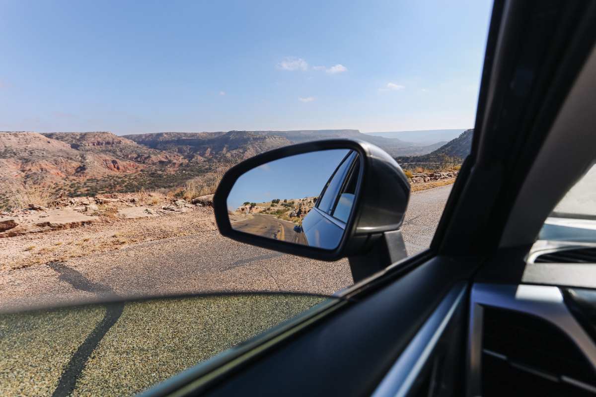 Estrada vista pelo retrovisor de um carro em movimento, simbolizando atenção e segurança nas viagens durante o Carnaval.