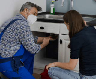 Encanador consertando uma pia e conversando com uma mulher