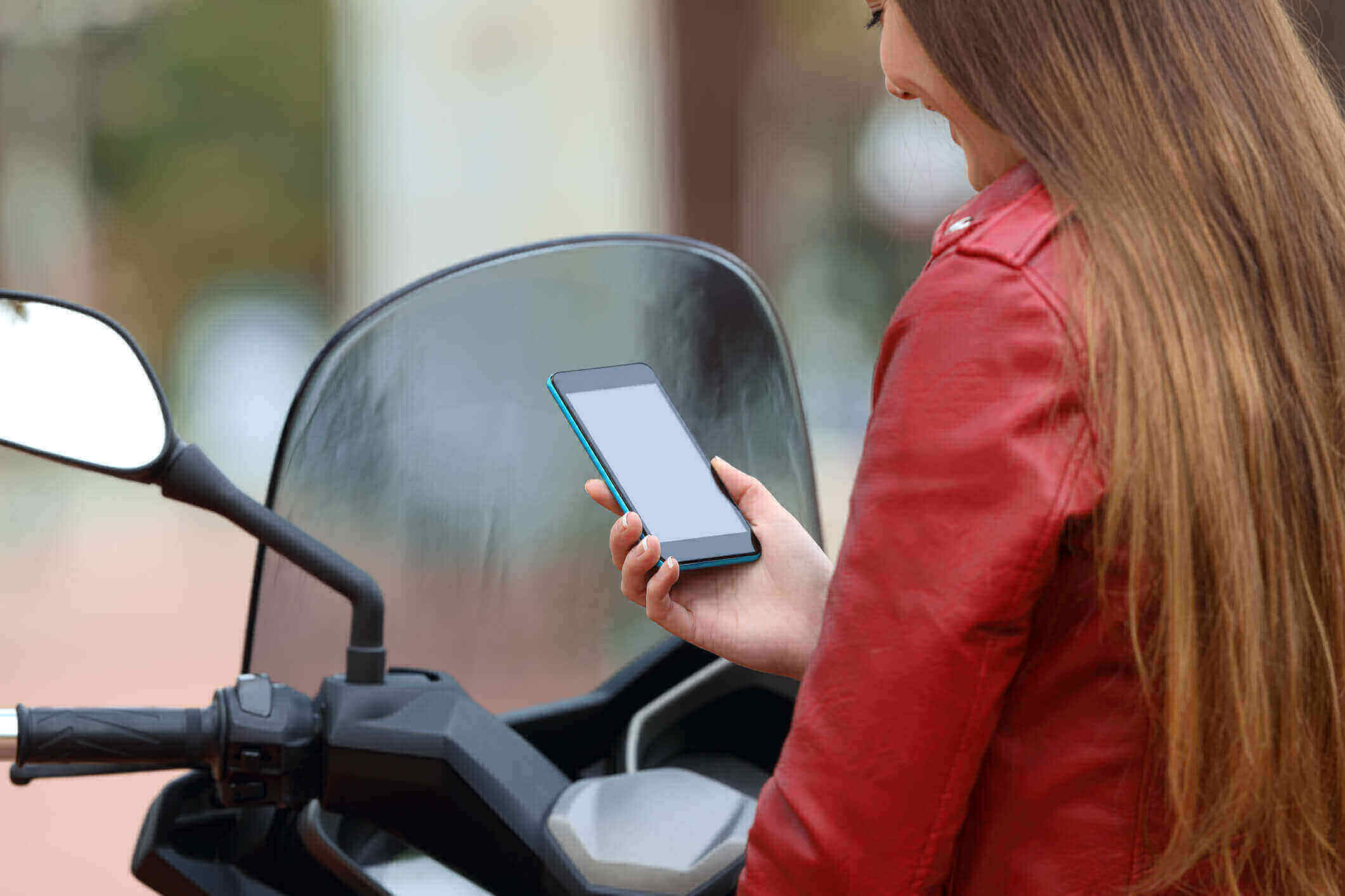 Motociclista em cima da sua moto utilizando o celular e sorrindo