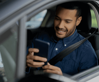 Homem sorrindo e utilizando o celular dentro do automóvel 