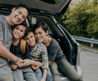 Família posando para foto se abraçando sentados no porta malas do automóvel