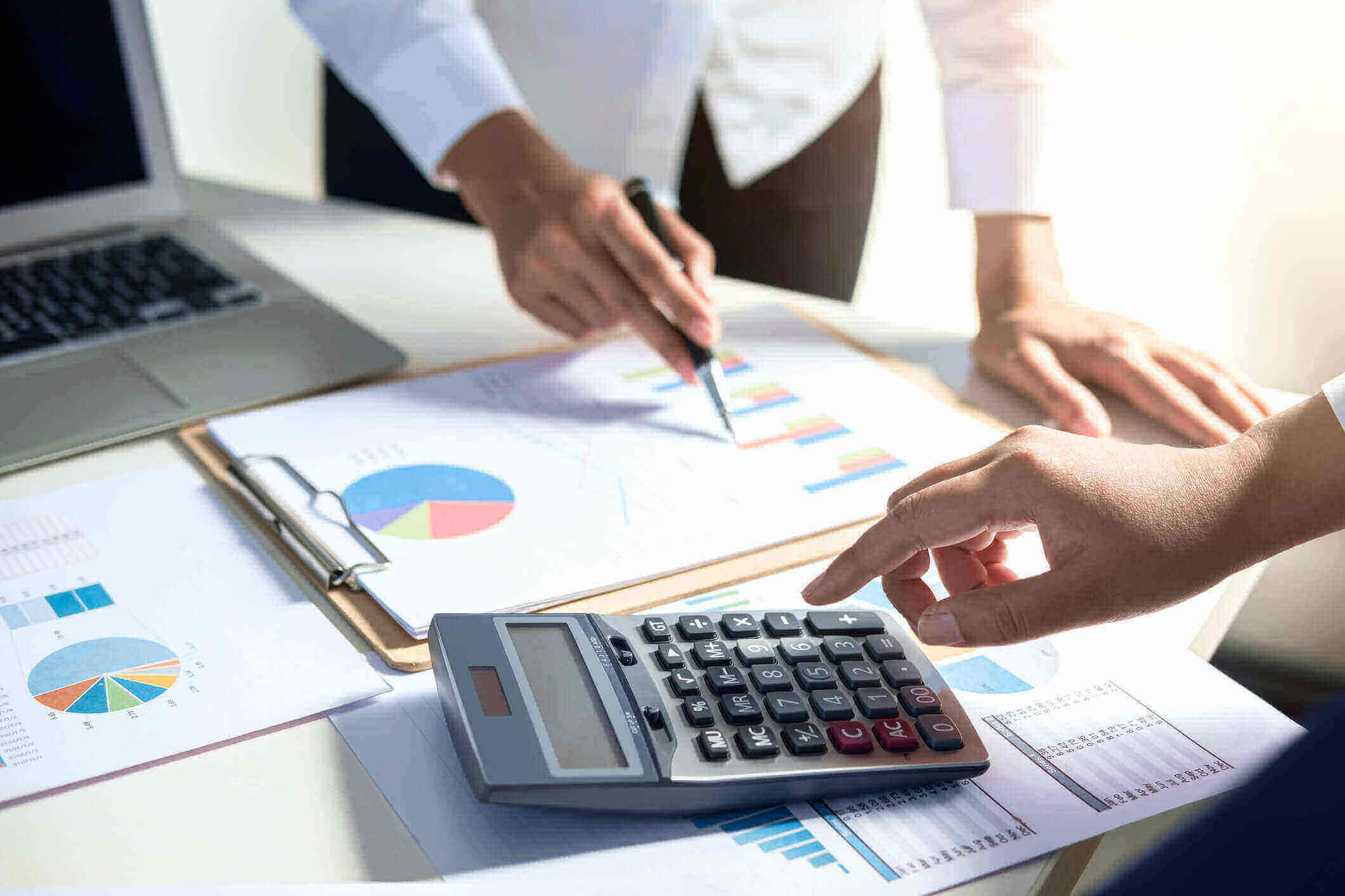 Duas pessoas analisando gráficos financeiros com uma calculadora em mesa de escritorio.