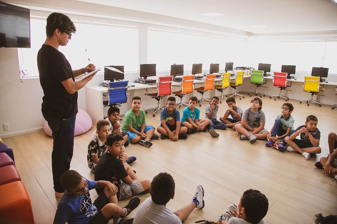 Professor de associação beneficente em sala de aula cercados por um círculo de alunos sentados no chão