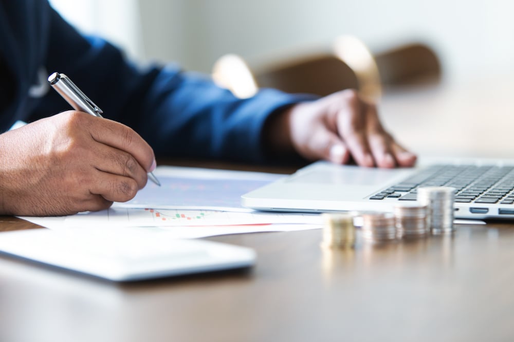 Homem no escritório fazendo análises de gráficos ao lado de uma pilha de moedas 