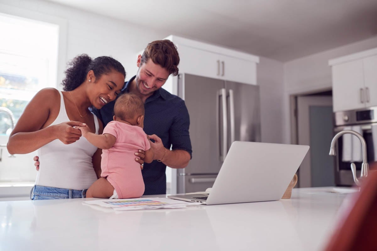 Familia sorridente com bebe apoiado em mesa com notebook ao lado.