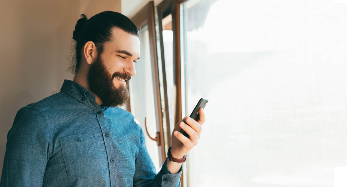 Homem com uma camisa azul utlizando o celular e sorrindo
