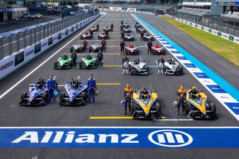 Carros de Fórmula 1 enfileirados com seus respectivos pilotos ao lado, em frente ao logo da Allianz