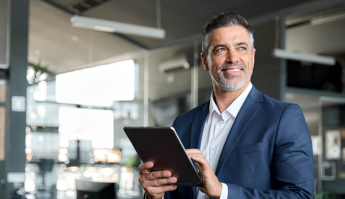 Homem de meia idade, usando terno, segurando um tablet e sorrindo