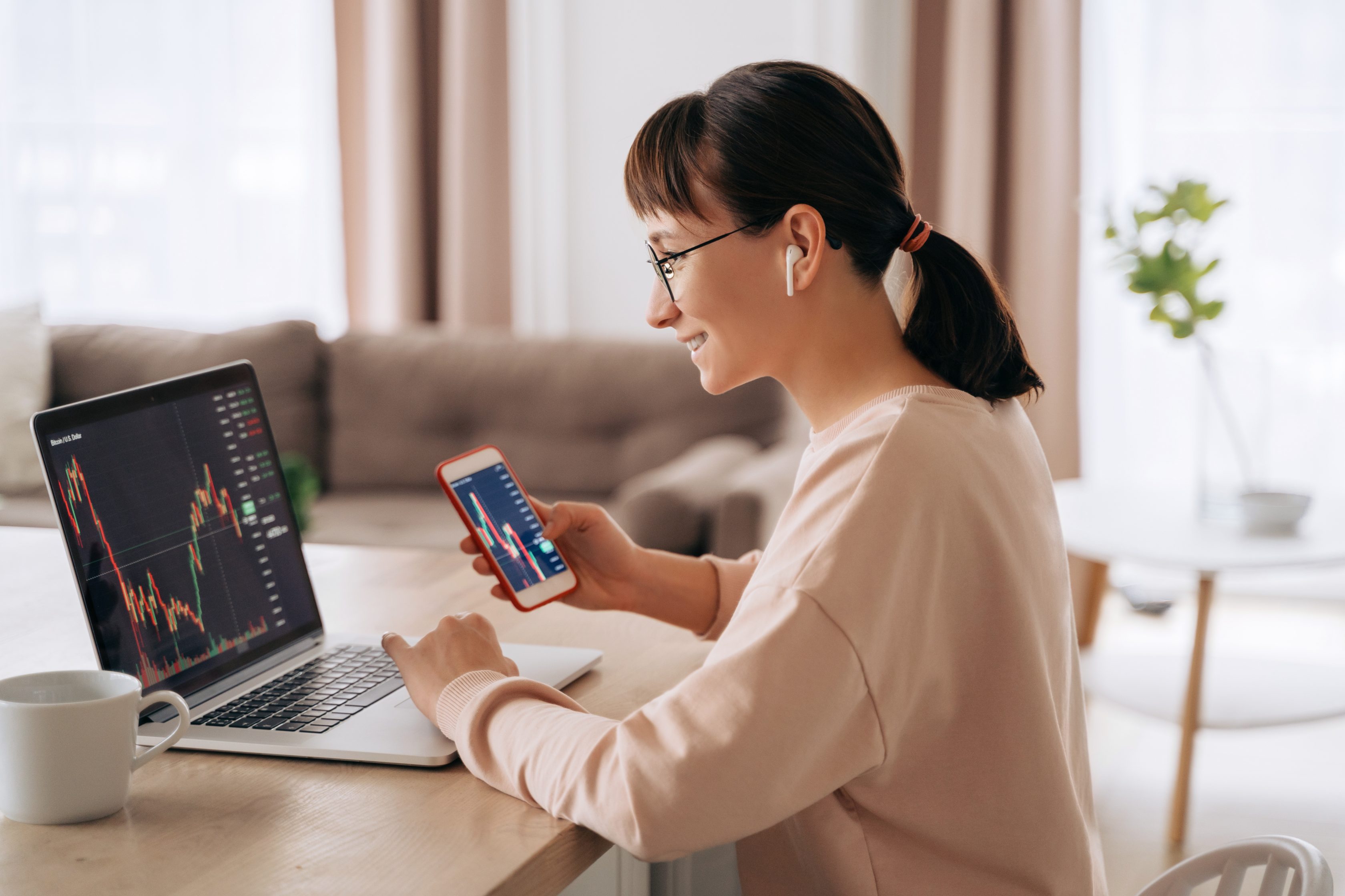 Mulher usando fones de ouvido e analisando um gráfico no seu computador e celular