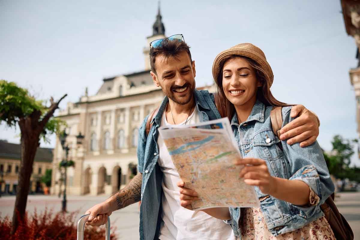 Casal sorridente em viagem segurando um mapa.