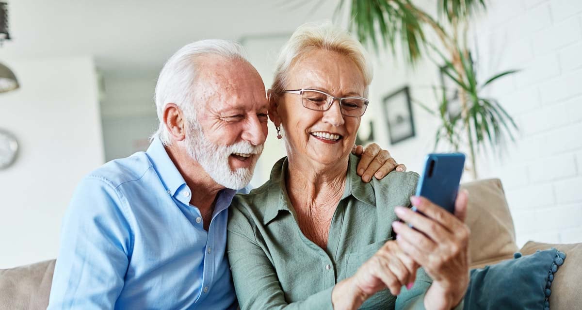 Casal de idosos sorridentes usando um celular.