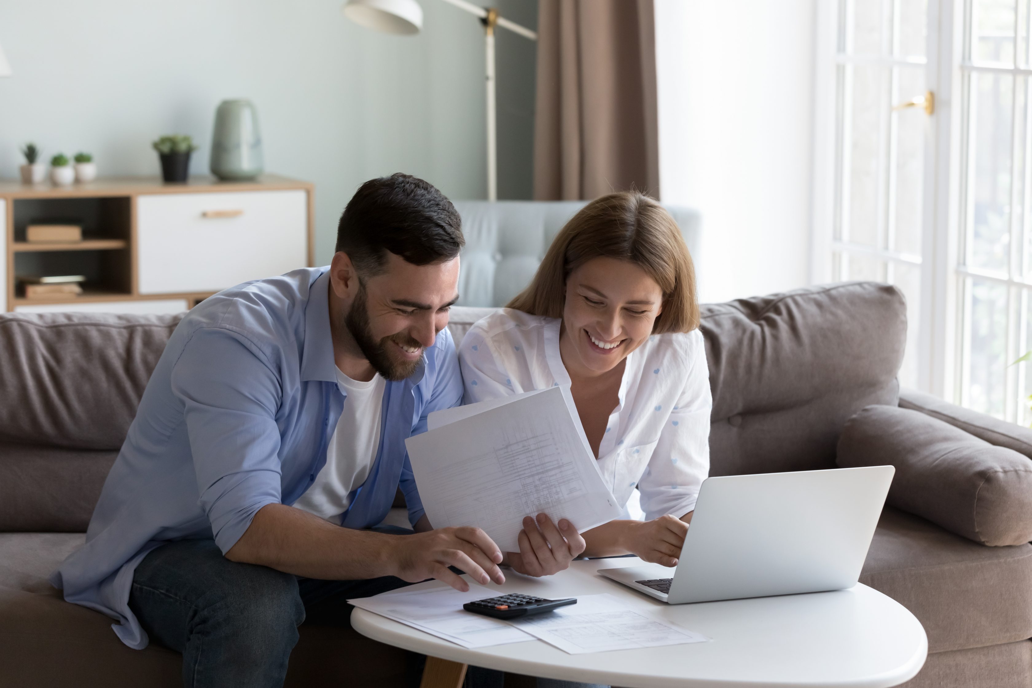 Casal feliz usando um notebook ao lado de uma calculadora.