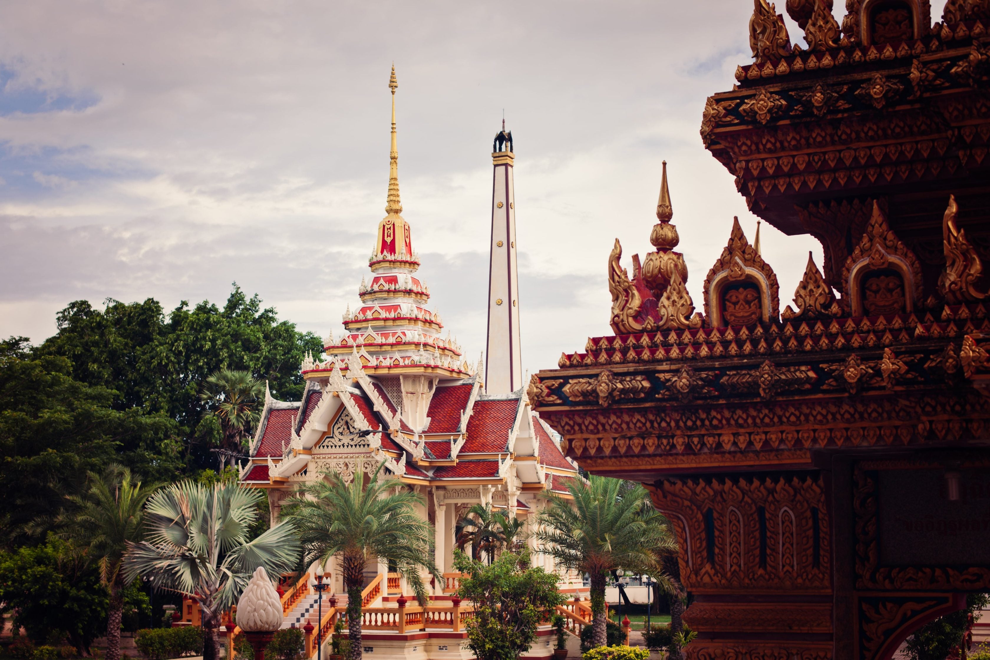 Vista de templos tailandeses tradicionais com torres e arvores ao redor.