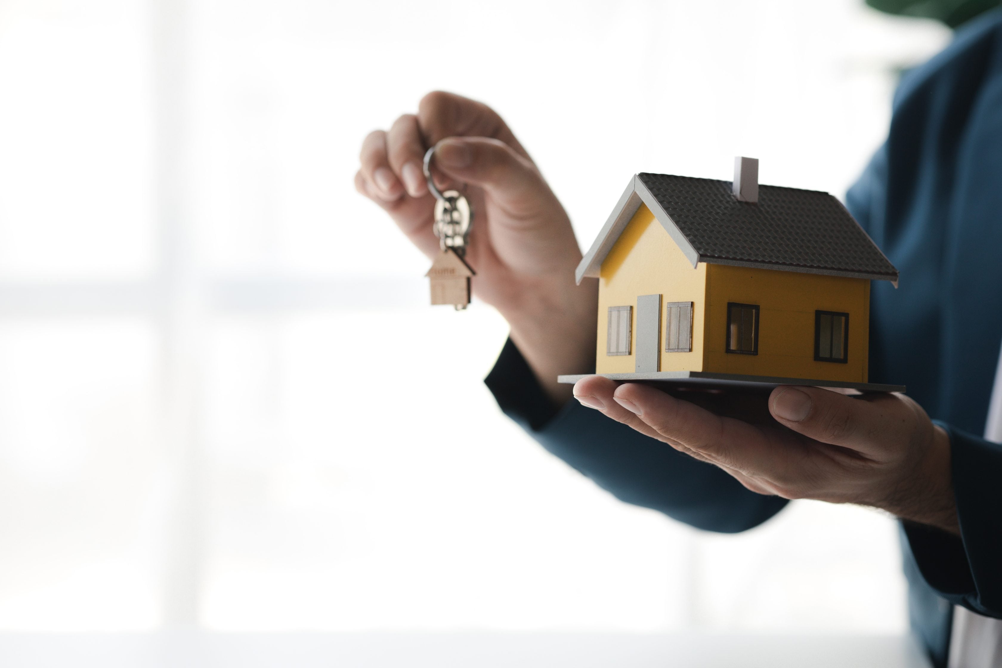 Homem segurando uma miniatura de casa e as chaves.