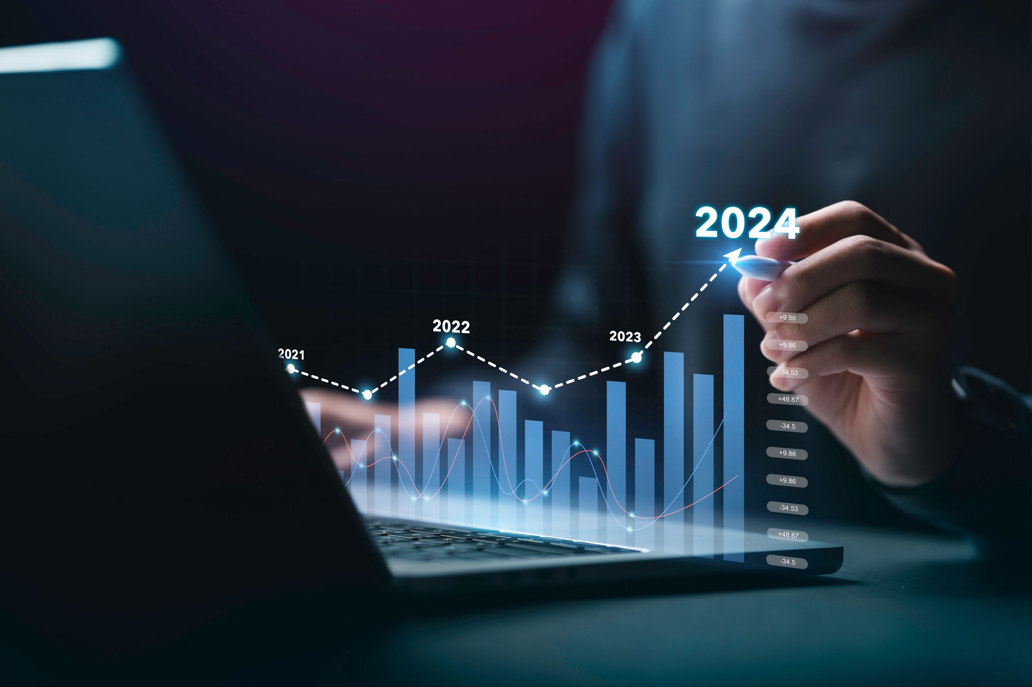 Homem usando notebook com gráfico digital flutuante apontando crescimento no ano de 2024.