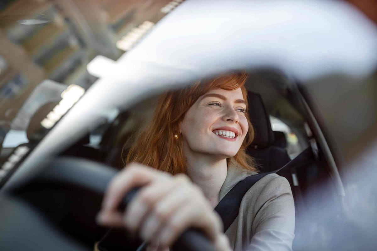 Mulher dirigindo com expressão de satisfação, representando as novas coberturas e assistências do seguro Auto Allianz.