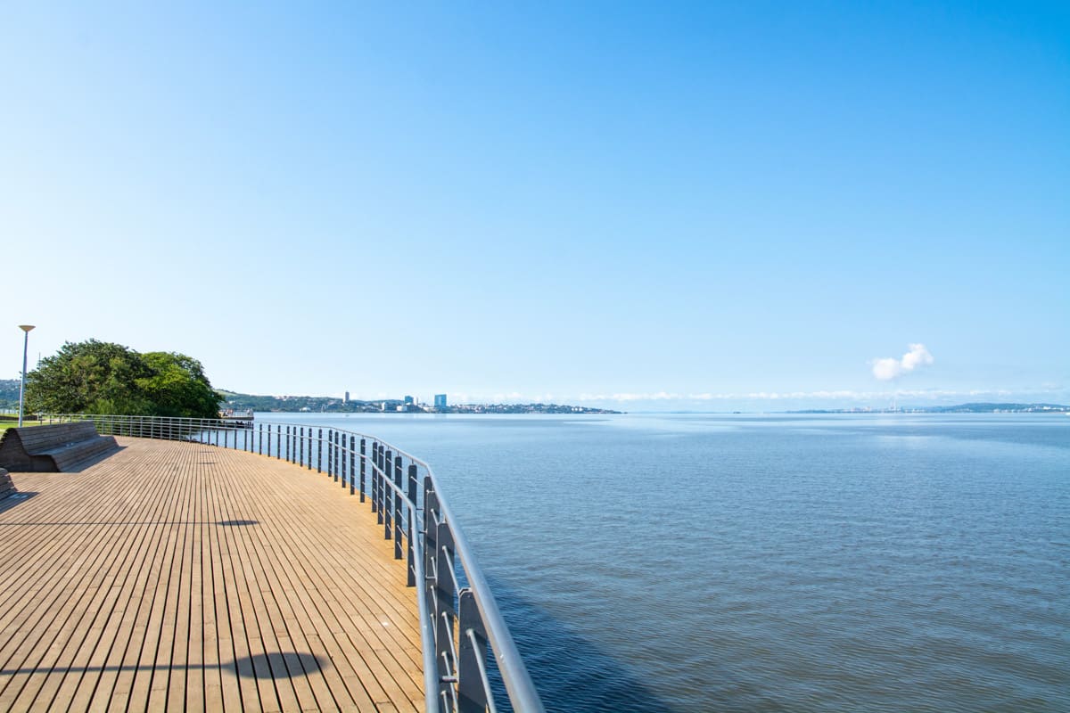 Calçadão à beira do Guaíba em Porto Alegre, com skyline sob céu azul.